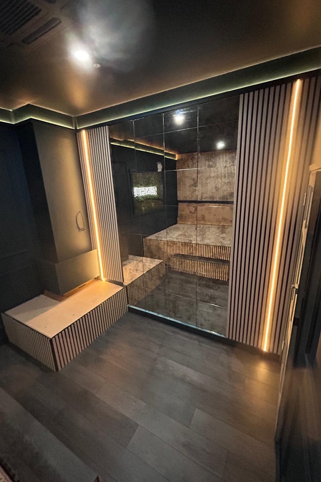 Modern steam room with glass walls and wooden benches in a dimly lit setting.