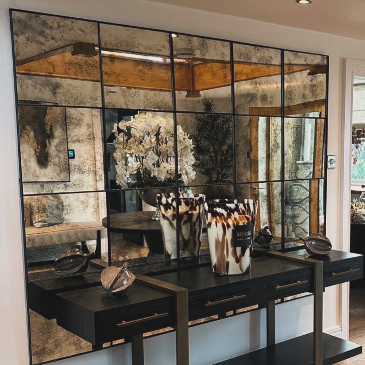 Twenty panel steel framed antique mirror spanning a wall behind a dark counter and florals