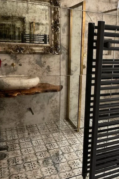 Black towel radiator in a bathroom with patterned tiles and mirrors.