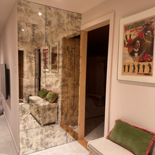 Antique mirror tile feature wall in a hallway beside a green upholstered bench