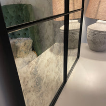 Satin black steel framed antique mirror beside a pale ceramic lamp