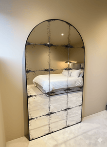 Constantine arch antique mirror leaning on bedroom carpet, reflecting a made bed