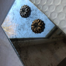 Antique mirror tile sample shown with silver and gold decorative rosettes