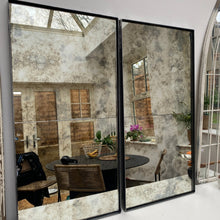 Two panel steel framed antique mirror leaning in a dining room, reflecting shuttered windows