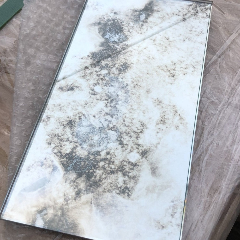 Single antique mirror tile sample showing hand-aged foxing across the glass